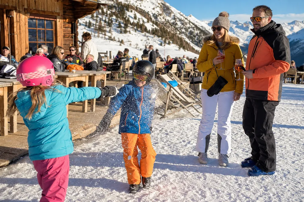 Barn i skidhjälm leker i snön utanför en bergrestaurang